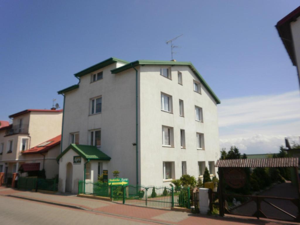 a white building with a green fence on a street at APARTAMENT i pokoje Aura Dom Wczasowy in Darlowko