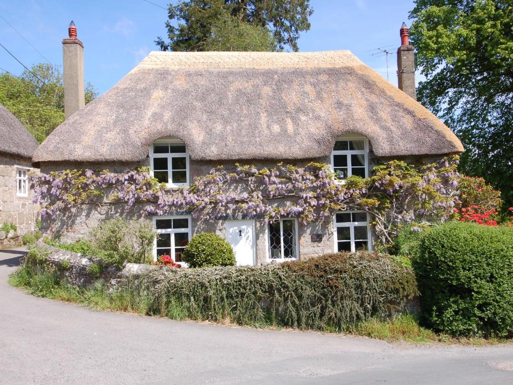 a thatch roof house with flowers on it at Thorn Cottage in Chagford