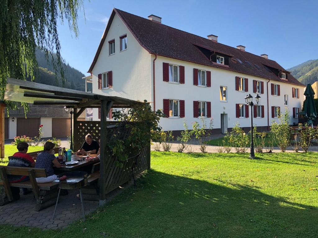 a group of people sitting at a table in front of a house at Apartmenthaus Pastner am Teich in Übelbach