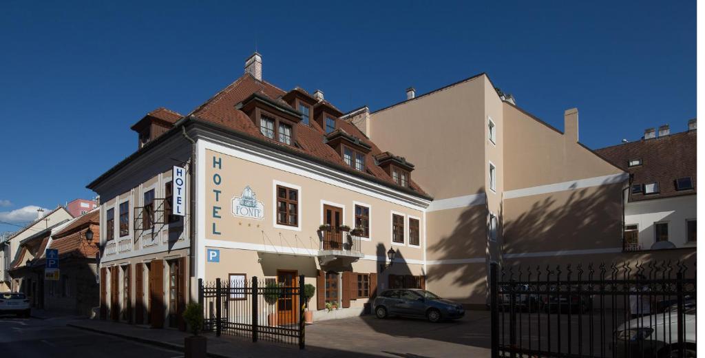 a white building with a red roof next to other buildings at Fonte Hotel in Győr