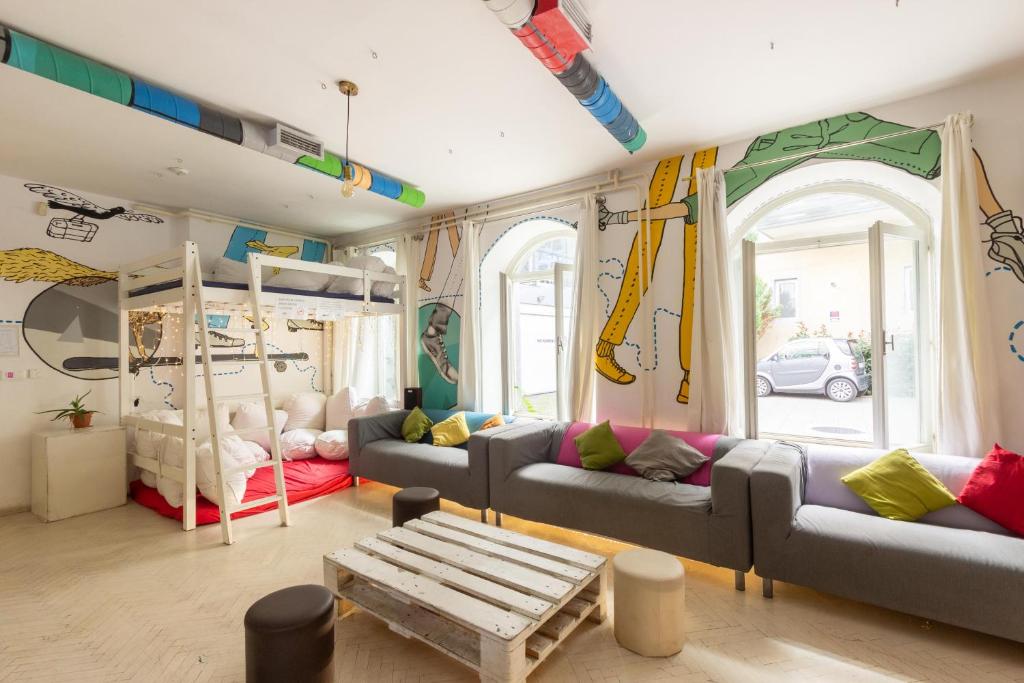 Communal lounge with white bunk beds, colorful travel-style mural, gray sofas, wooden coffee table and street-facing windows at Whole Wide World Hostel in Zagreb