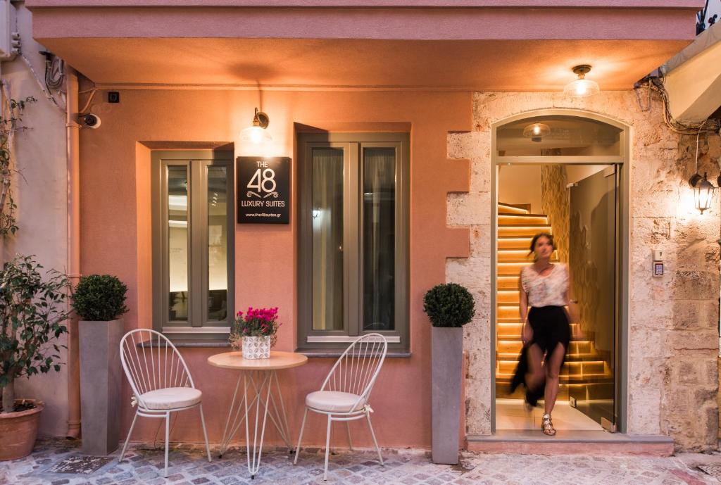 a woman walking outside of a building with a table and chairs at The48suites in Chania Town