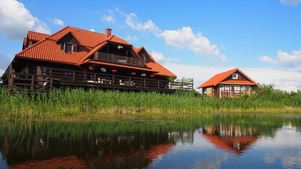a house with a red roof sitting next to a lake at Dwór Łabędzie w Kiermusach in Kiermusy