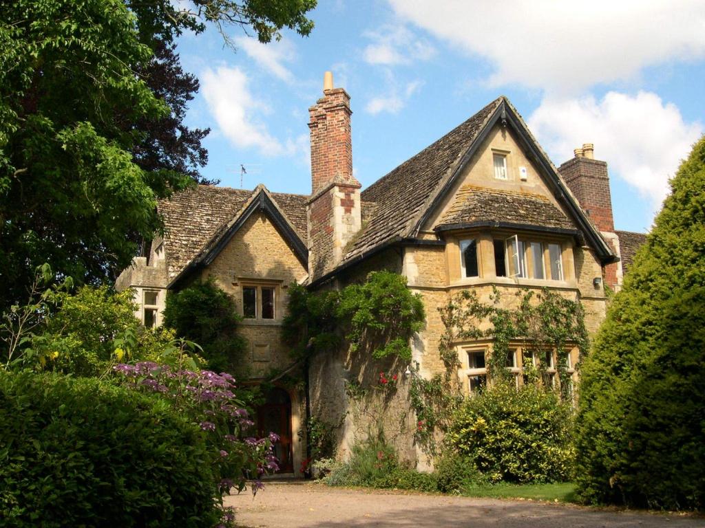 una antigua casa de piedra con chimenea y arbustos en Lullington House, en Frome