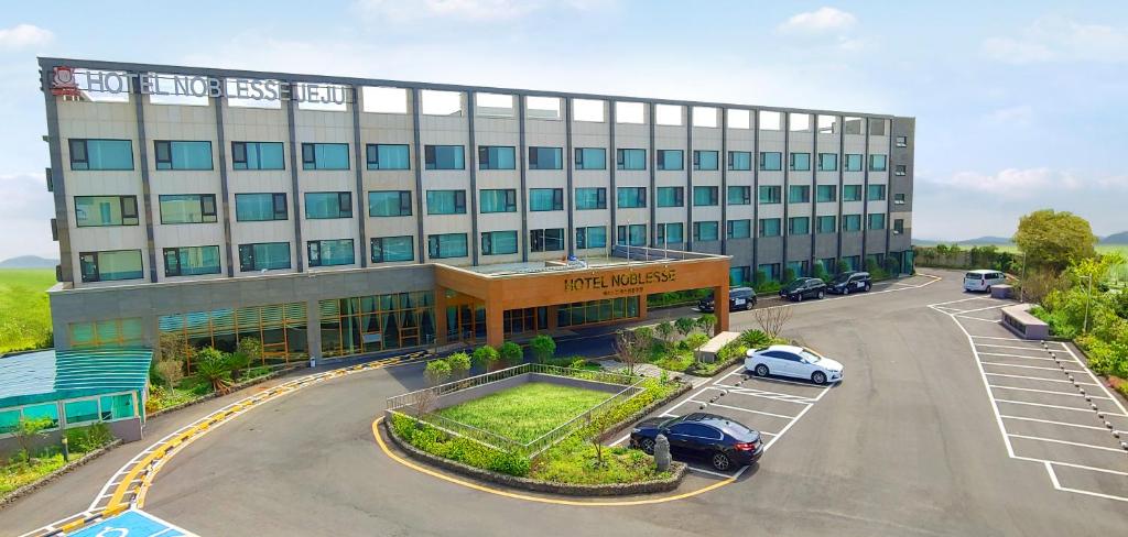 ein großes Gebäude mit Autos auf einem Parkplatz in der Unterkunft Jeju Noblesse Hotel in Jeju-do