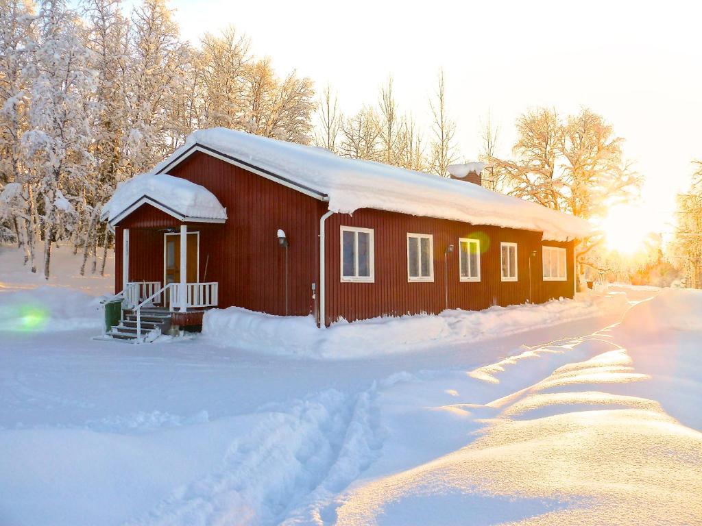 un piccolo edificio coperto di neve con il sole dietro di Stora Björnstugan a Laisvall