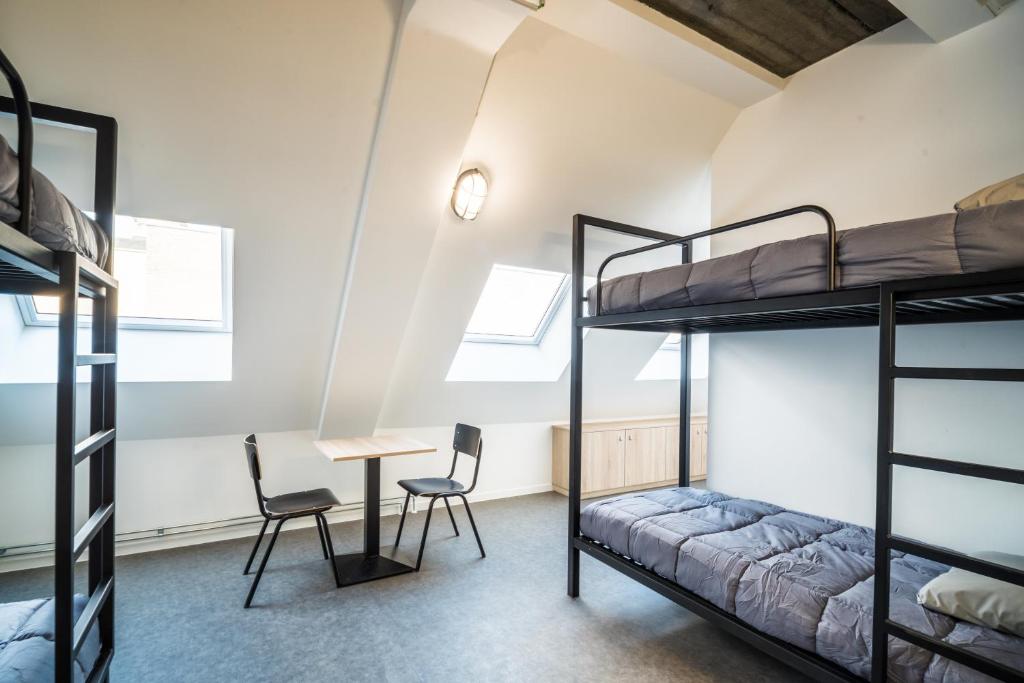 シャルルロワにあるAuberge de Jeunesse Charleroi Youth Hostelの二段ベッド、テーブル、椅子が備わる客室です。