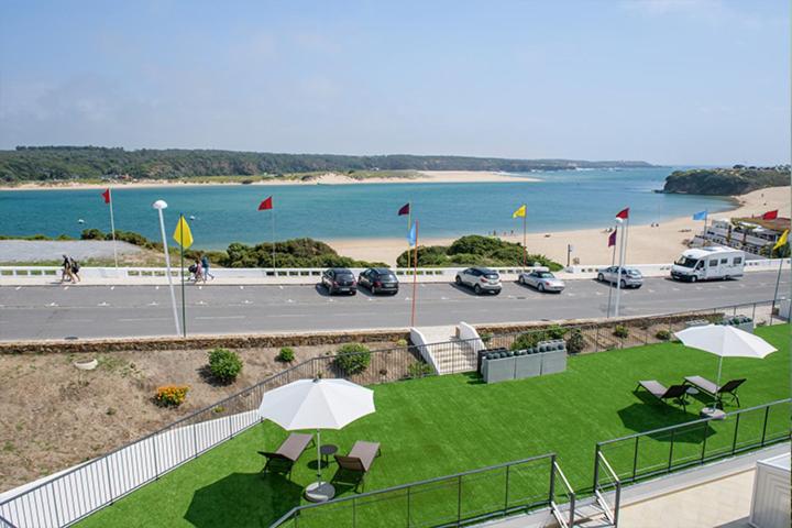 une pelouse avec des parasols et un parking avec une plage dans l'établissement Cerca da Vitoria 3 Milfontes, à Vila Nova de Milfontes