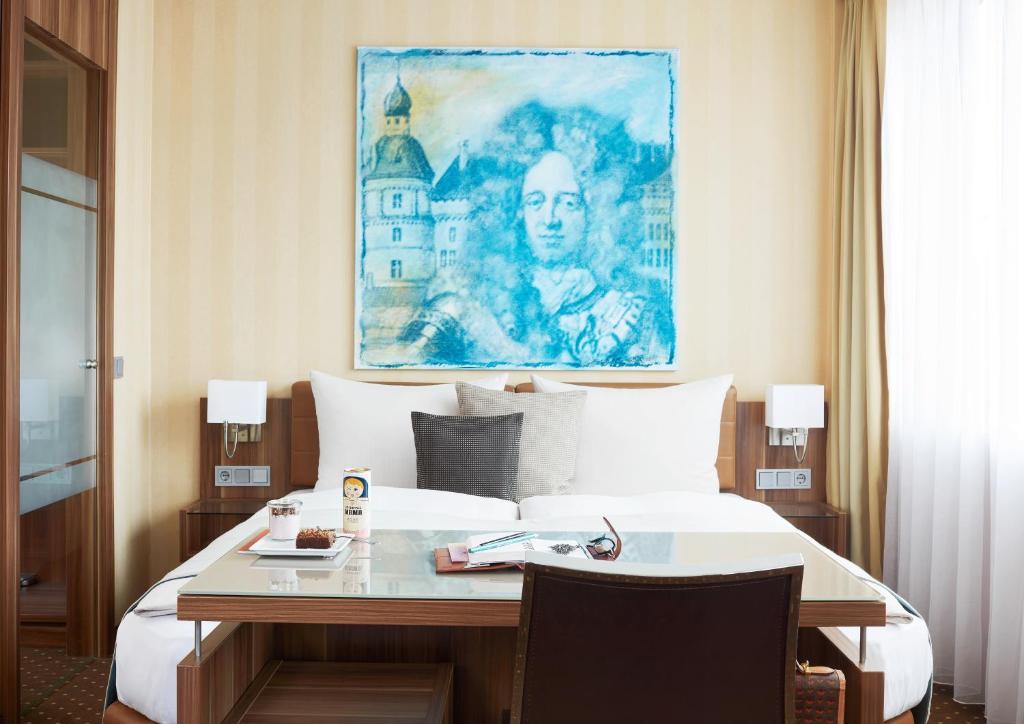 Una habitación de hotel con una cama con un escritorio y un cuadro. en Living Hotel Düsseldorf, en Düsseldorf