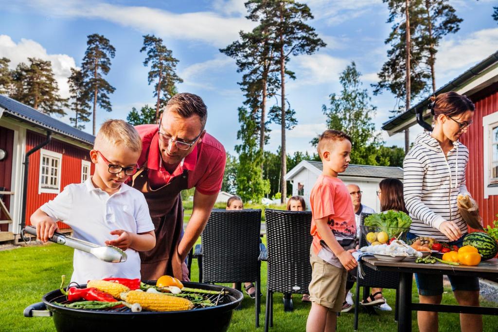 um homem e crianças à volta de uma grelha com vegetais em Kronocamping Lidköping em Lidköping