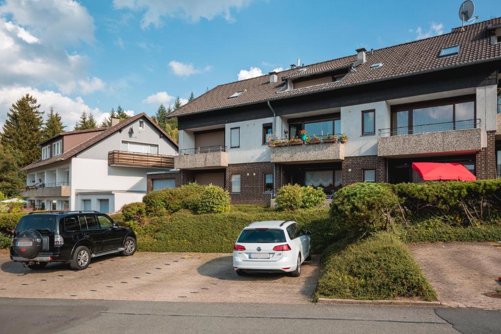 2 voitures garées sur un parking en face d'un immeuble dans l'établissement Ferienwohnung Harzblick, à Lautenthal