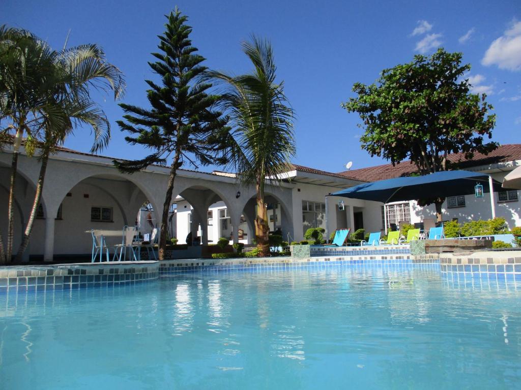 a swimming pool in front of a house with palm trees at Blue Lagoon Lodge Blantyre in Blantyre
