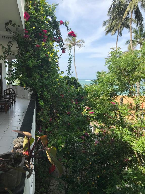 a balcony of a house with flowers and palm trees at Unawatuna Beach Bungalow - in Unawatuna