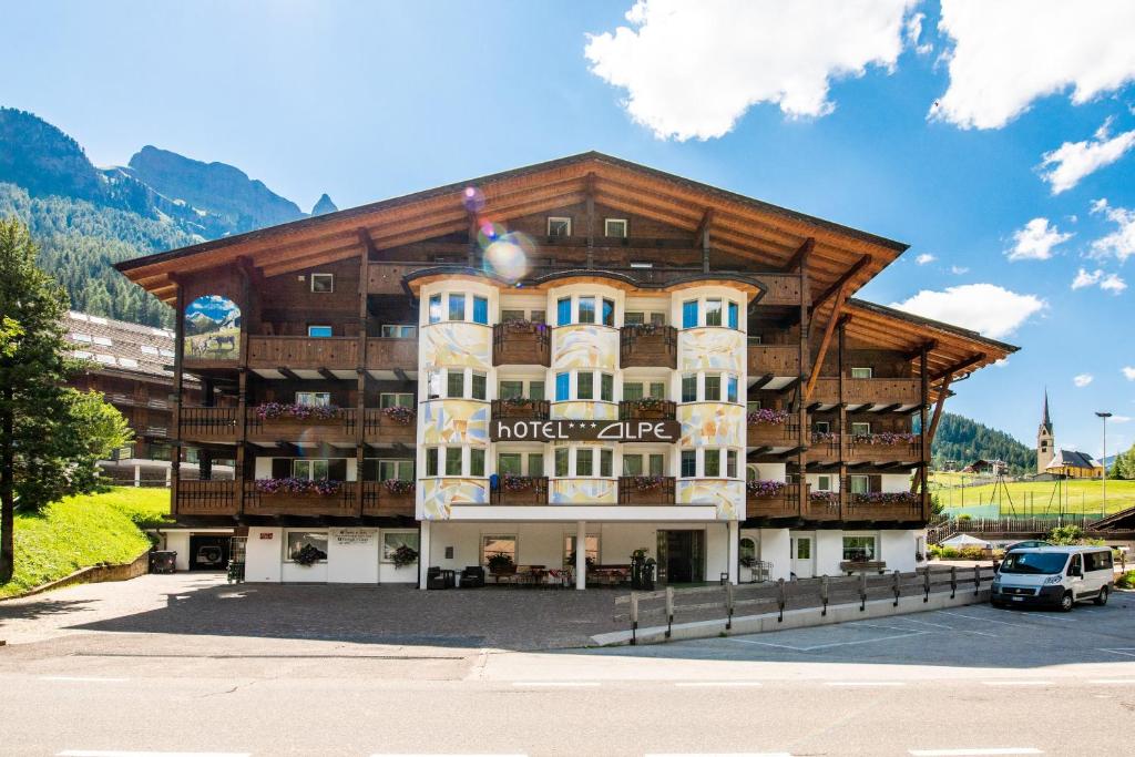 a large building in a parking lot next to a mountain at Hotel Alpe in Canazei