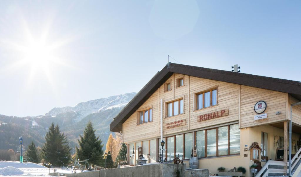 ein großes Holzgebäude mit Bergen im Hintergrund in der Unterkunft Hotel-Restaurant Ronalp in Bürchen