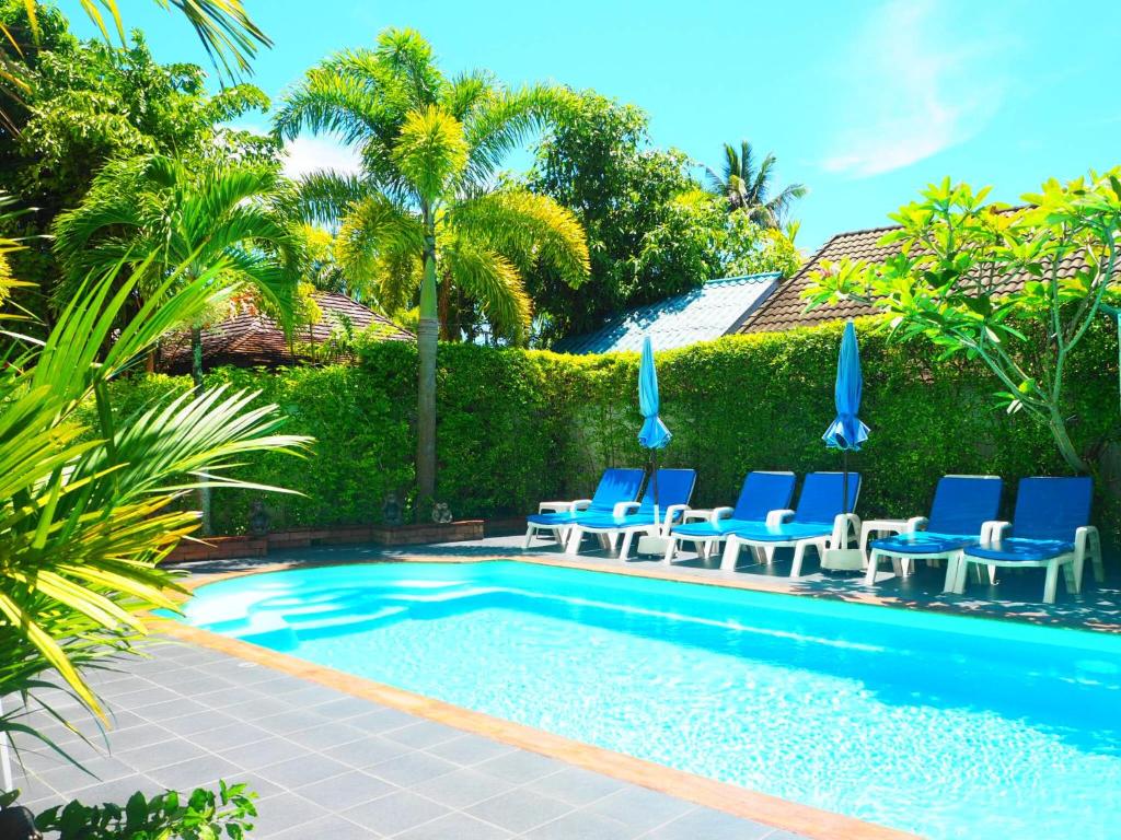 a swimming pool with blue chairs and palm trees at Baan Rosa Bangtao Beach in Bang Tao Beach