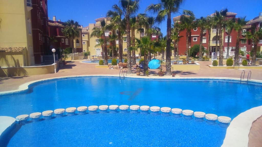 a large blue swimming pool with palm trees and buildings at Beautiful 3 bed, 2 bath modern apartment in Los Alcázares