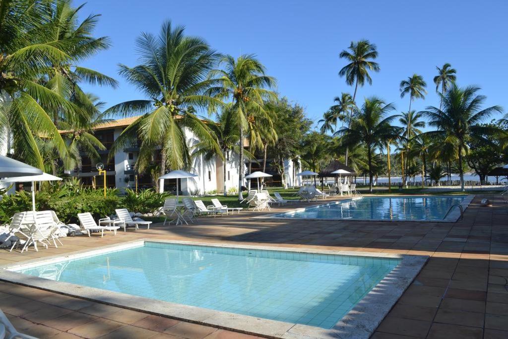 a swimming pool with palm trees and a resort at Casa Sol e Mar Beira-mar in Ilhéus