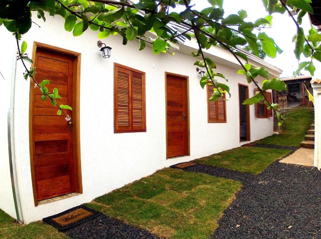 a white building with wooden doors and grass at Pousada Sempre Viva in São João Batista do Glória