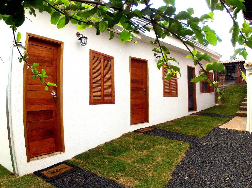 un edificio blanco con puertas de madera y césped en Pousada Sempre Viva, en São João Batista do Glória