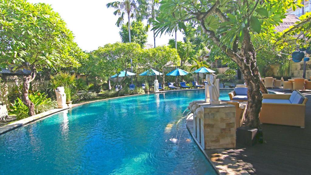 a swimming pool in a resort with trees and umbrellas at The Amasya in Seminyak