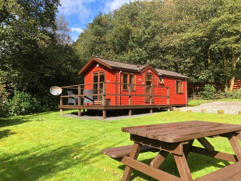 a red cabin with a picnic table in front of it at Rashfield Sheilings - Riverside Lodges, by Pucks Glen, Dunoon in Dunoon
