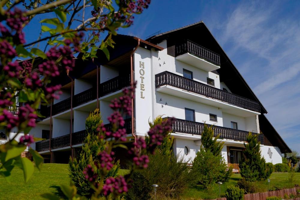 a white building with a black roof and some flowers at Garni Hotel & Ferienwohnungen Seeschlößchen in Waldeck