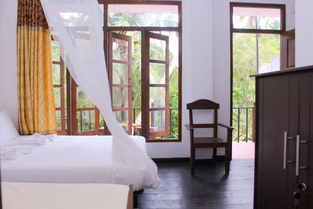 a bedroom with two beds and a chair and windows at wood palace mirissa in Mirissa