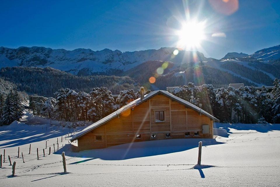 a wooden cabin in the snow with the sun at Chalet du champ Martel in Villard-de-Lans