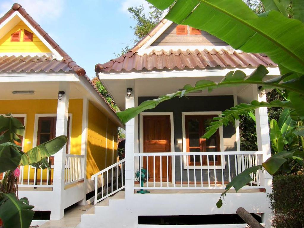 een klein huis met een witte veranda en geel bij Thiw Tara Resort in Nakhon Nayok