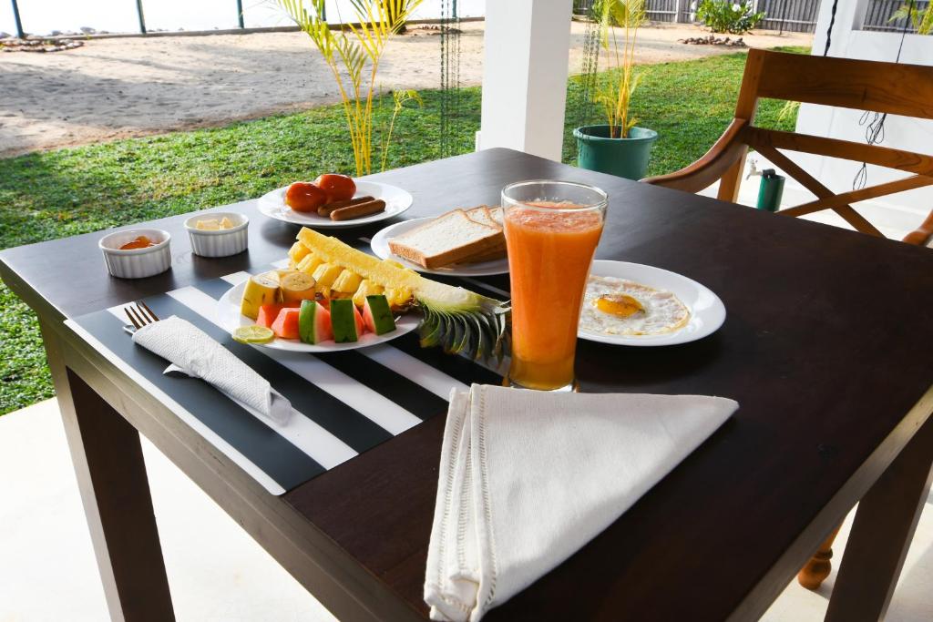a table with plates of food and a glass of orange juice at The Araliya Retreat in Kalpitiya