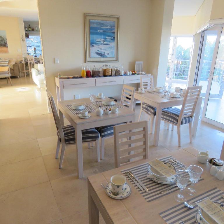 a dining room with two tables and chairs with dishes on them at Gull on the Bay Boutique Guest House in Bloubergstrand