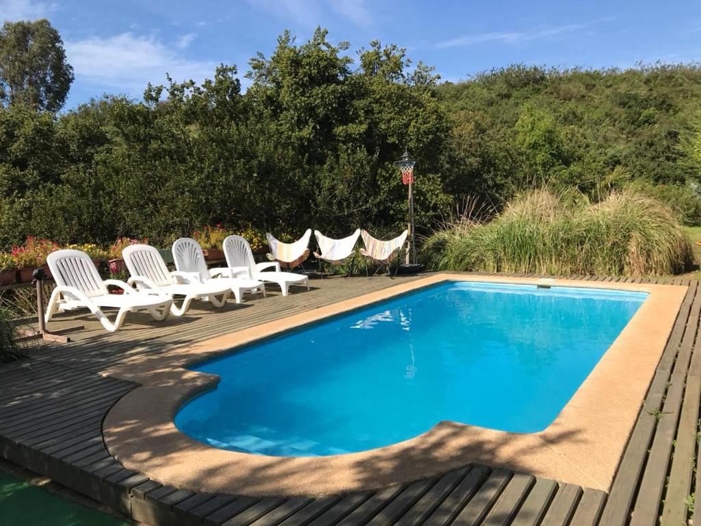 una piscina con 2 sillas blancas junto a una terraza de madera en Parcela Los Castaños, en Concón