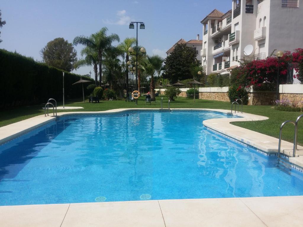 a large blue swimming pool in a park with a building at Apartamento playa - Puerto Banus in Marbella