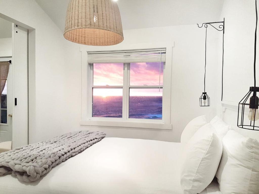 a white bedroom with a bed and a window at The Fish Sheds in Rocky Harbour