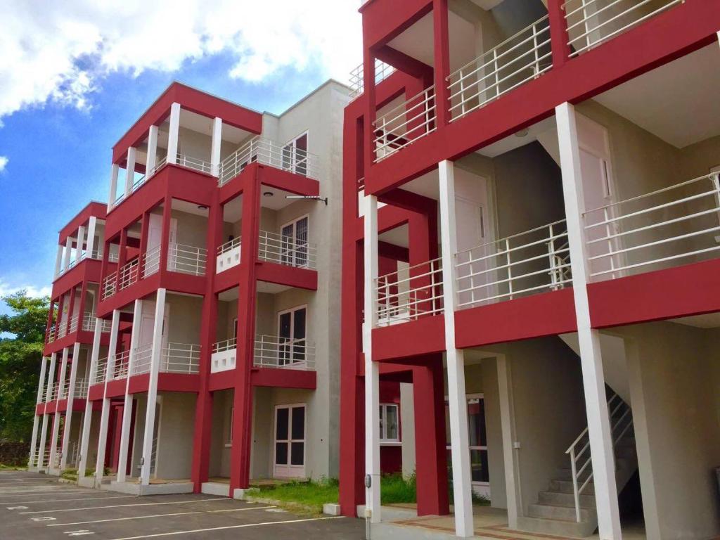 a red building with white balconies next to a parking lot at Pereybere Apartment in Pereybere