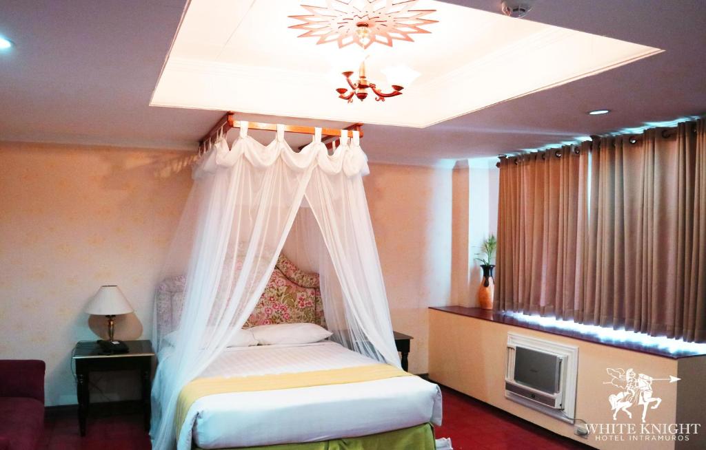a bedroom with a canopy bed and a tv at White Knight Hotel Intramuros in Manila
