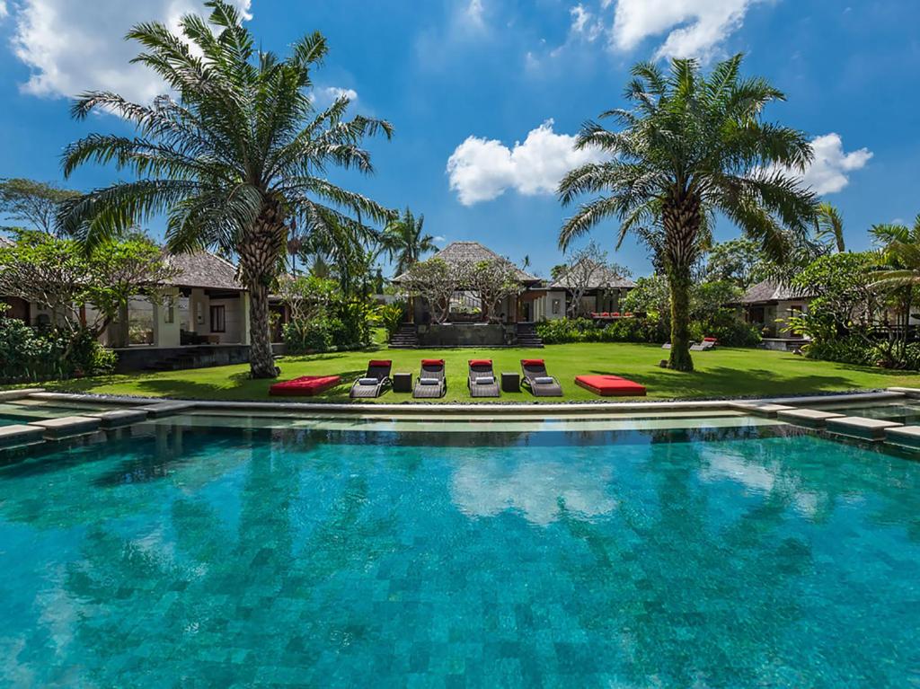 a swimming pool with chairs and palm trees at Villa The Beji in Canggu