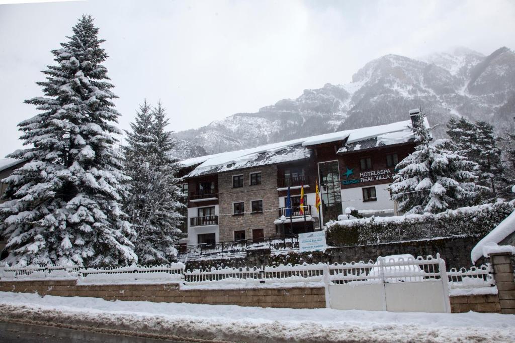 a snow covered building with a pine tree in front of it at Hotel & Spa Real Villa Anayet in Canfranc-Estación