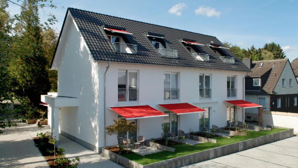 een wit huis met rode daken en planten bij Hotel Boskamp in Bergisch Gladbach