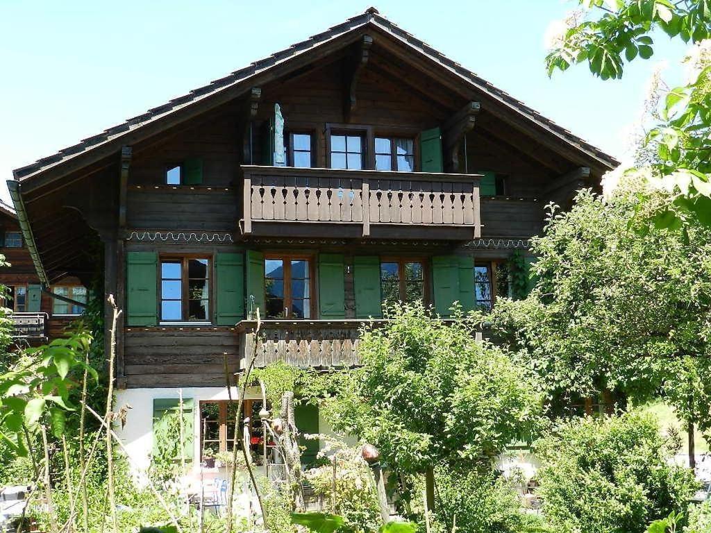 ein großes Holzhaus mit einem Balkon und Bäumen in der Unterkunft Apartment Im Wiesengrund by Interhome in Gstaad