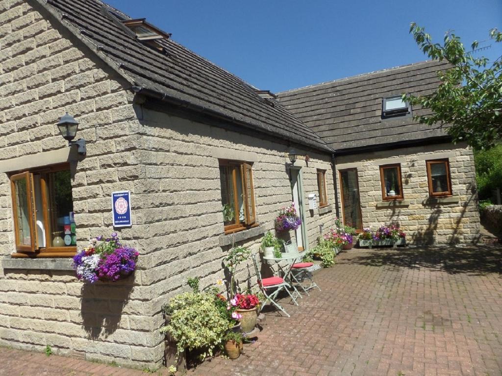 een stenen huis met stoelen en bloemen ervoor bij Innisfree Cottage in Eyam