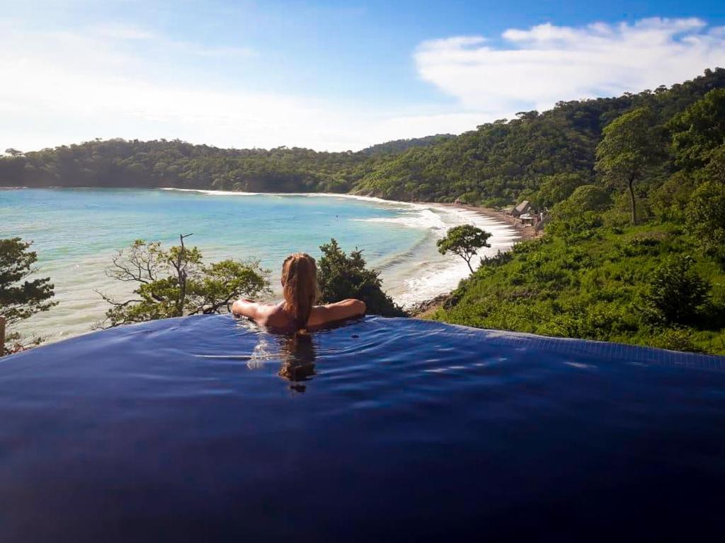 a woman sitting in a infinity pool overlooking a beach at Romantic Beachfront Retreat in San Juan del Sur
