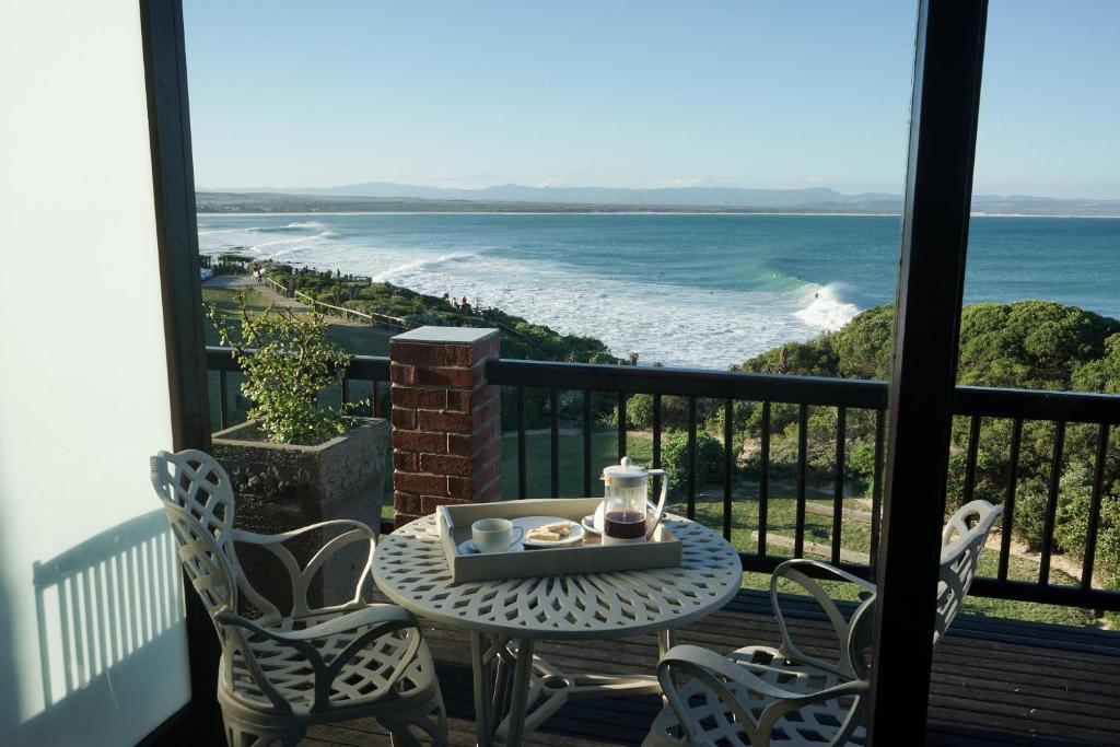 a table and chairs on a balcony with a view of the ocean at Shaloha Guesthouse on Supertubes in Jeffreys Bay