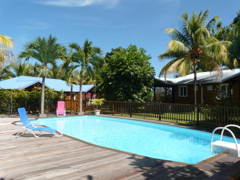 a pool with a deck and a chair and palm trees at Gîtes LAMATELIANE in Capesterre-Belle-Eau