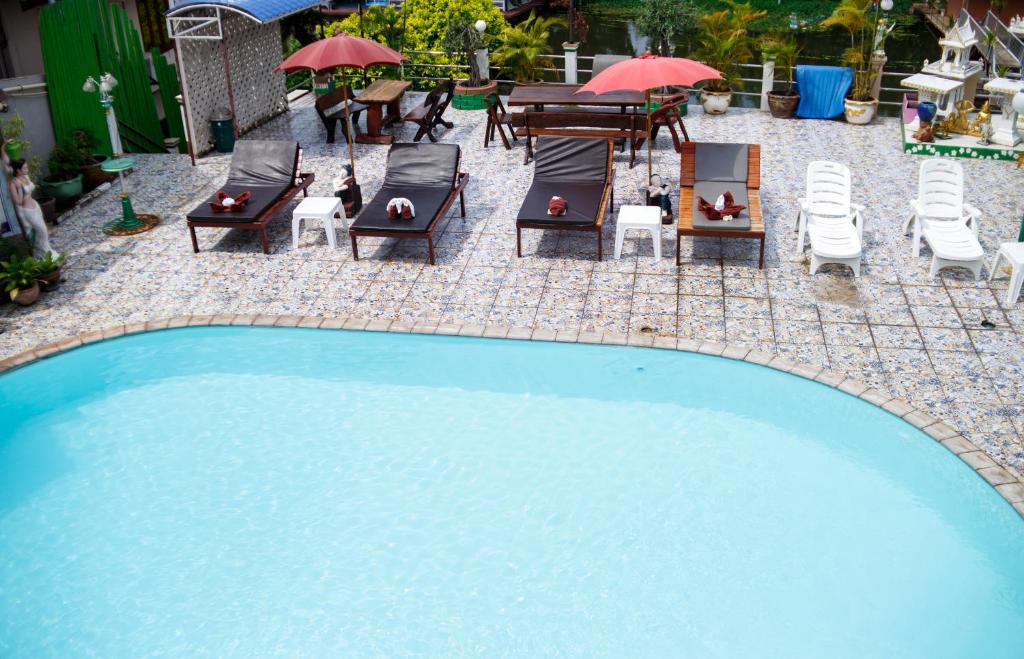 a swimming pool with chairs and tables and umbrellas at Noble Night Guesthouse in Kanchanaburi City