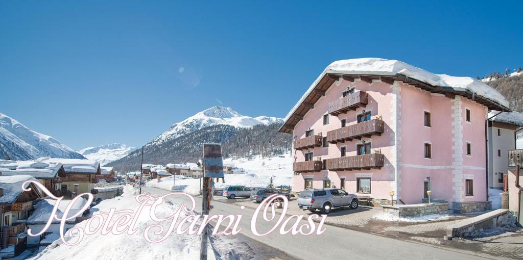 a pink building with a snow covered mountain in the background at Garni Oasi in Livigno