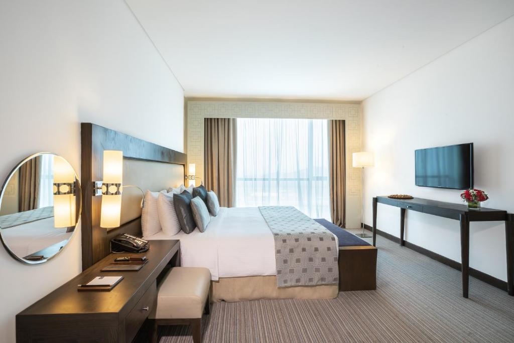 a hotel room with a bed and a desk and a mirror at Royal M Hotel Fujairah by Gewan in Fujairah