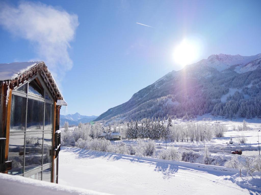 a house in the snow with a mountain in the background at Hôtel Restaurant Le Monêtier in Le Monêtier-les-Bains