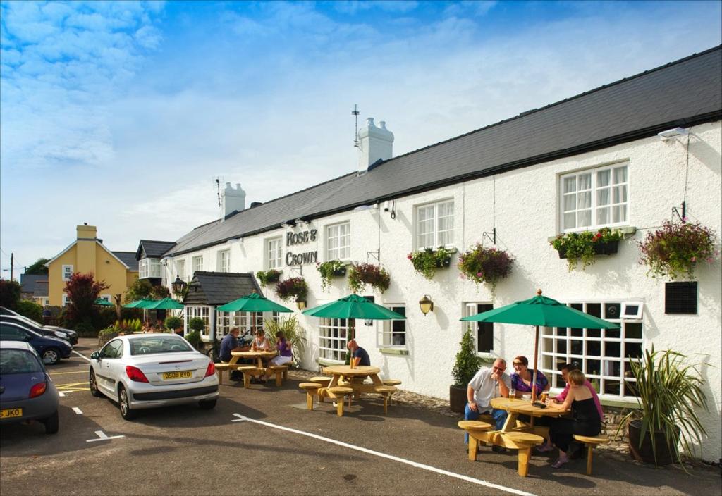 people sitting at tables outside of a building with green umbrellas at Rose And Crown in Porthcawl